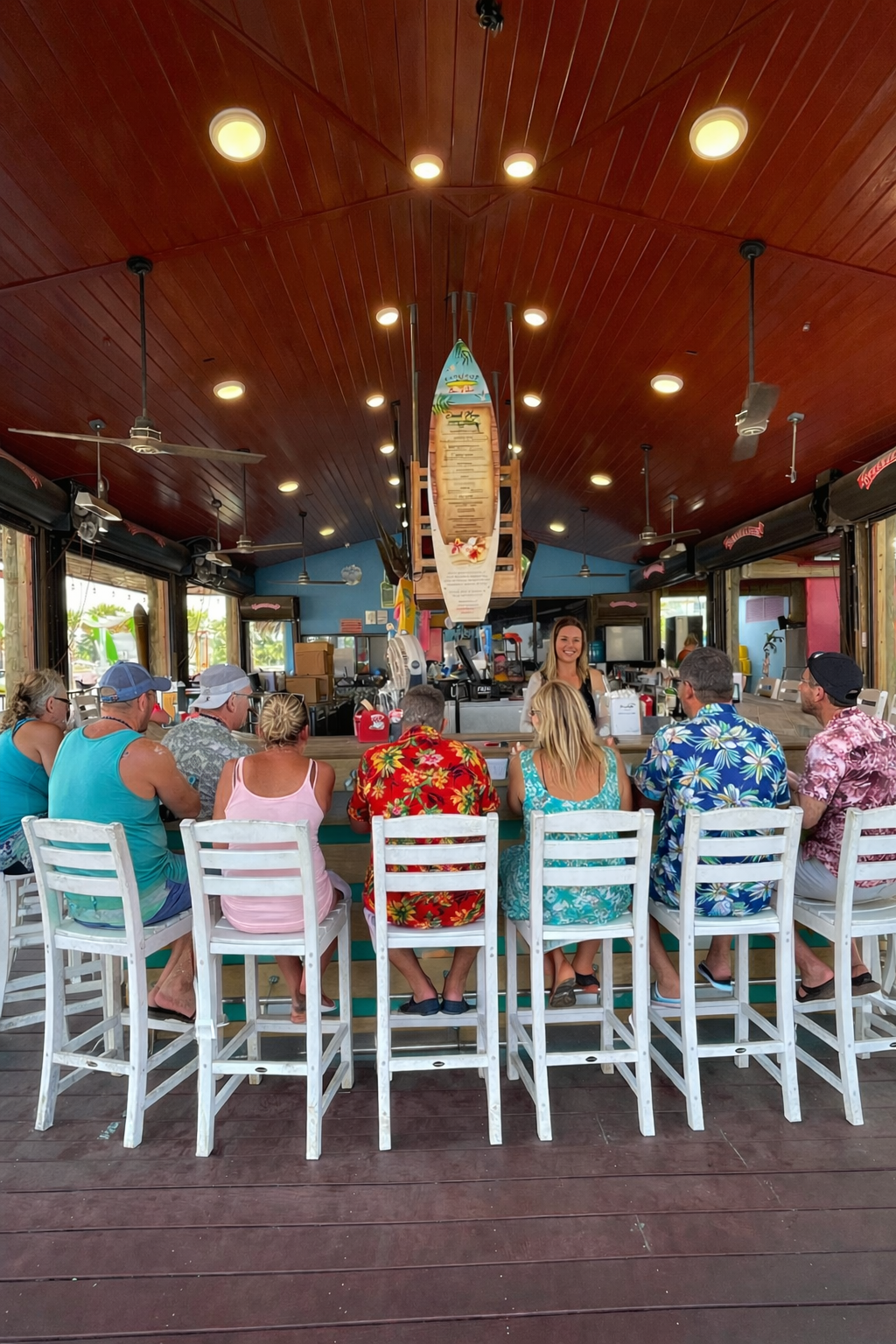 Guests sit at a vibrant bar, enjoying beach views, lively chatter, and a smiling server at Barefoot Restaurants.