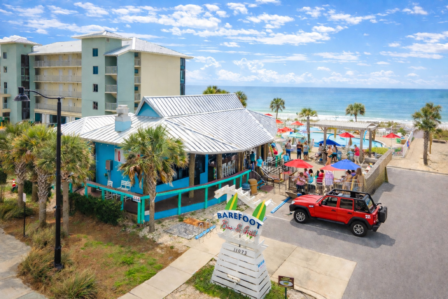 Guests gather at Barefoot Restaurants, enjoying Gulf views, colorful umbrellas, and lively beachfront dining.