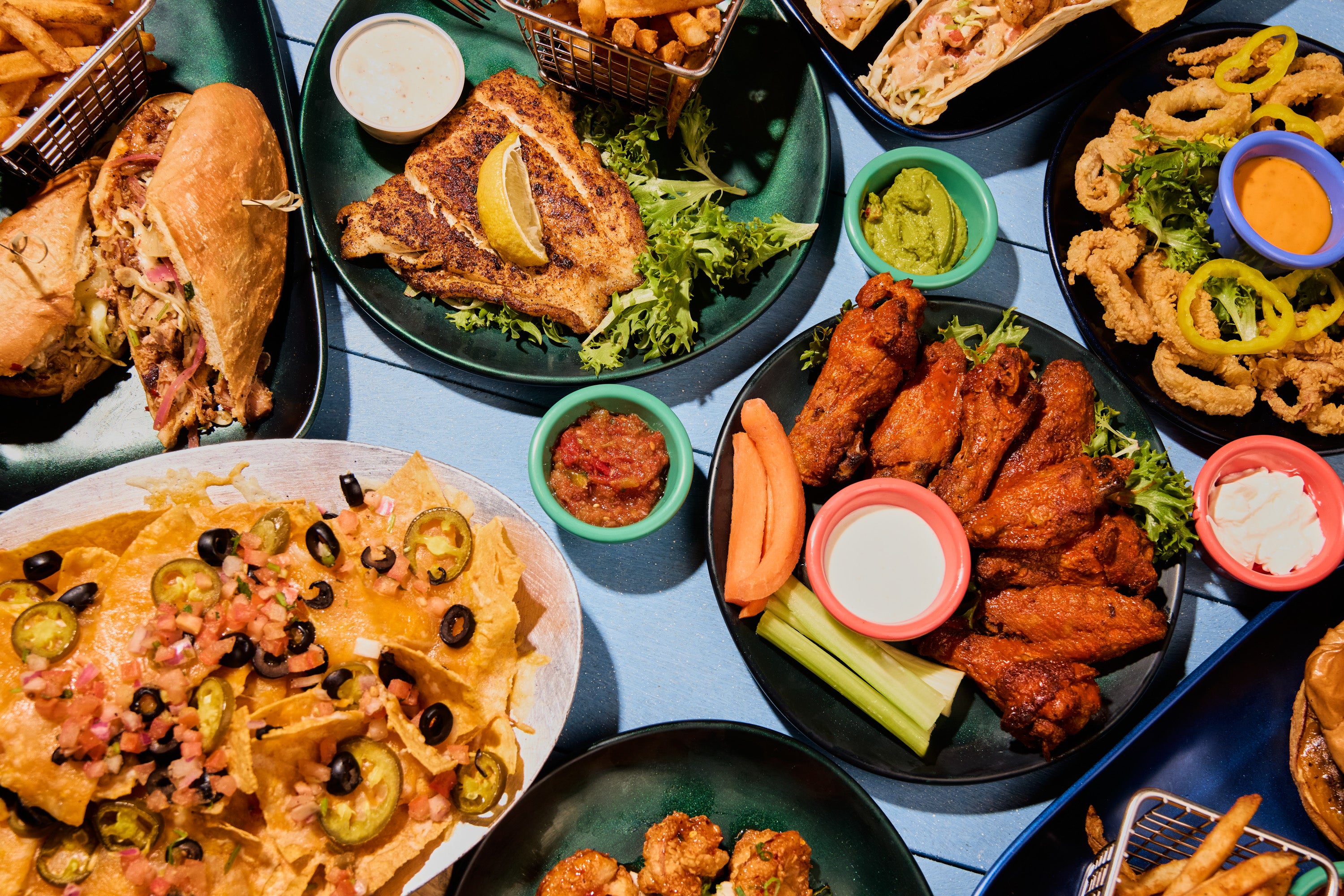 Colorful plates of seafood dishes and nachos beautifully arranged on a blue table at Barefoot Restaurants in Panama City Beach.