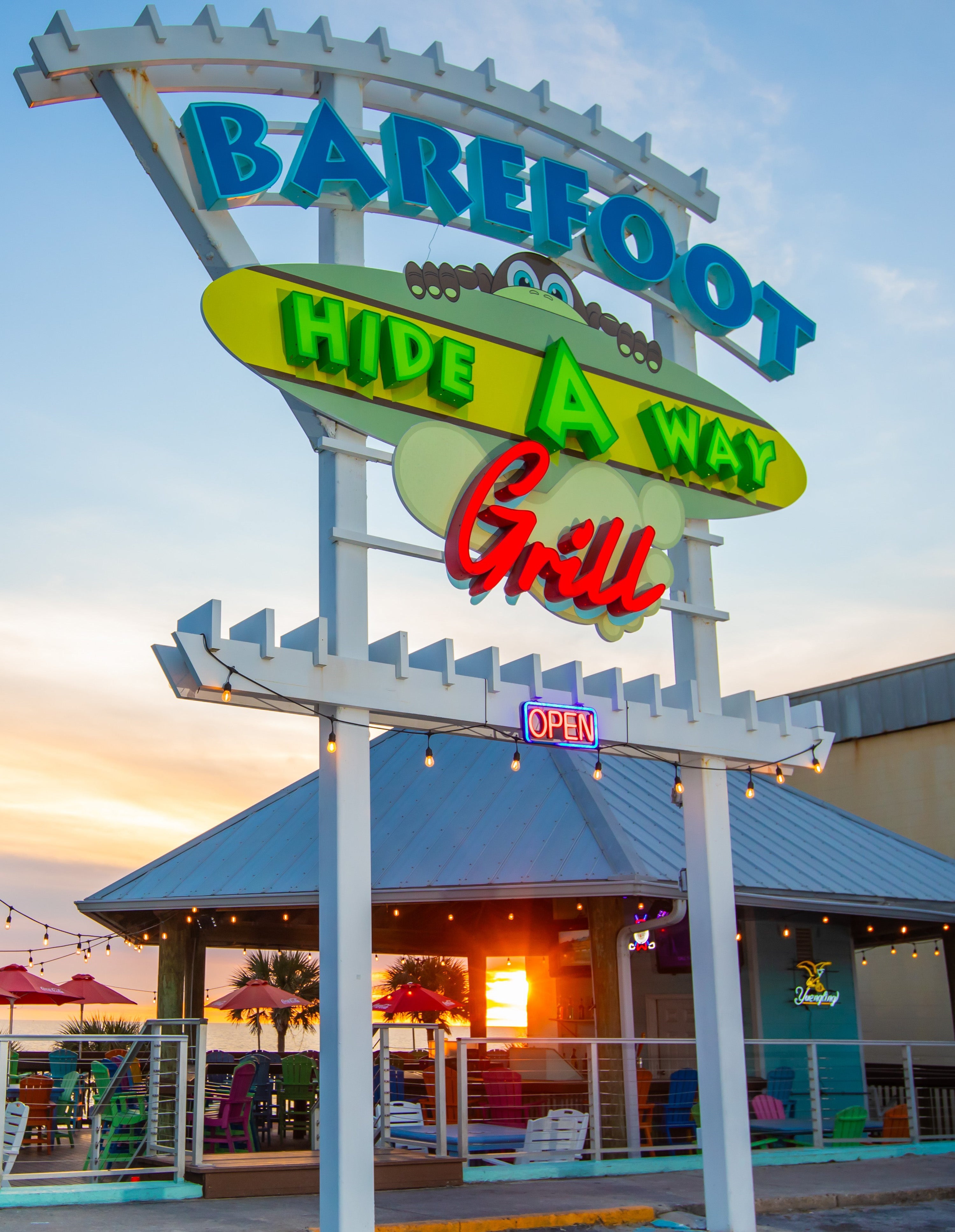Colorful sign at Barefoot Hide-A-Way glows as the sun sets, offering Gulf views and inviting beachfront dining.