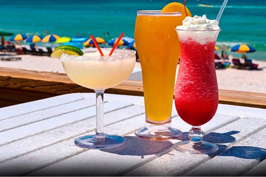 Colorful cocktails sit on a table, overlooking sun loungers and the Gulf at Barefoot Restaurants, Panama City Beach.
